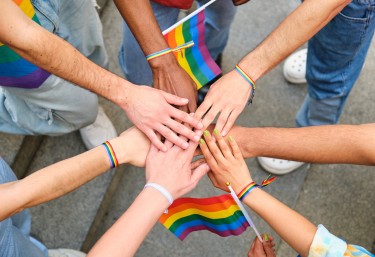 A group of people with rainbow bracelets on their hands. The people are of different races and genders and represent LGBTQ+