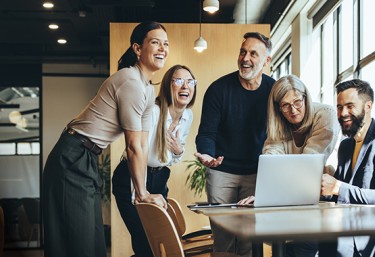 Women and men gathered around a table with a laptop